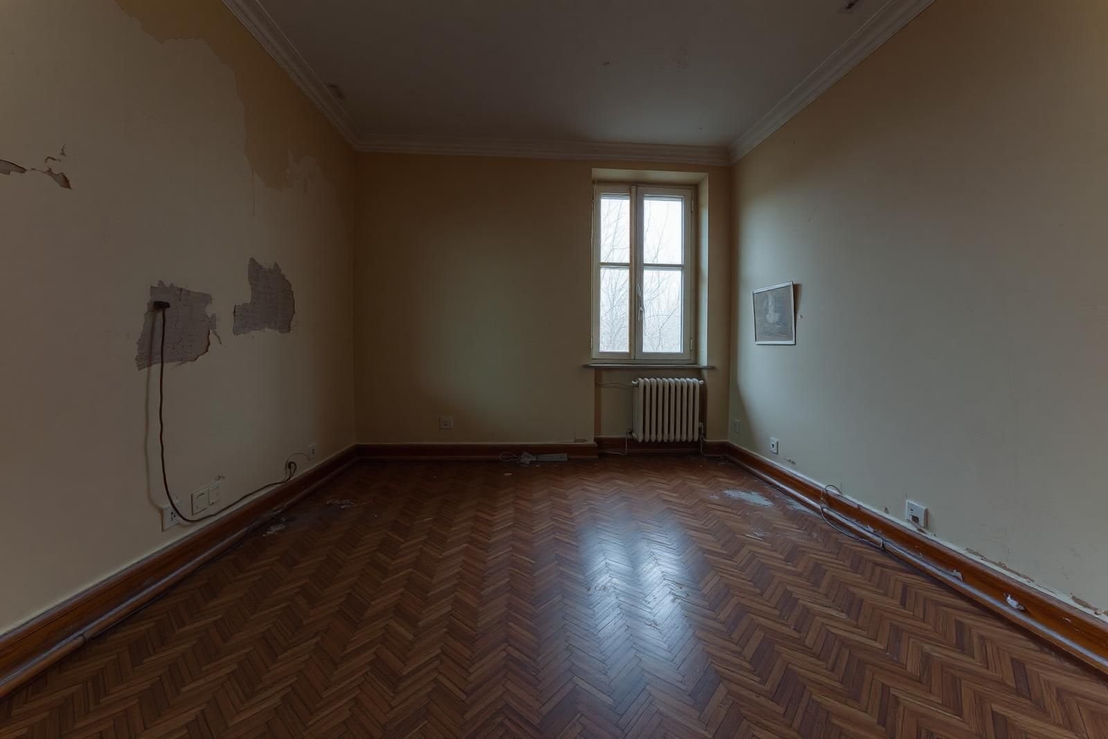 Altbauzimmer vor der Sanierung mit beschädigtem Parkett und abgenutzten Wänden